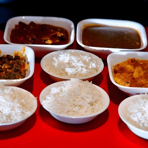 An Indian meal with various curries and rice served in white bowls on a red table.