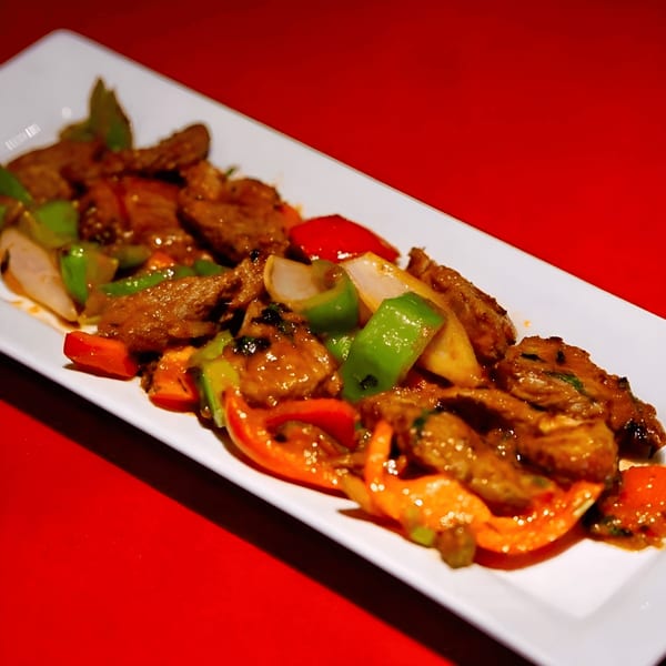 Indian stir-fried beef with red and green bell peppers and onions on a white platter.