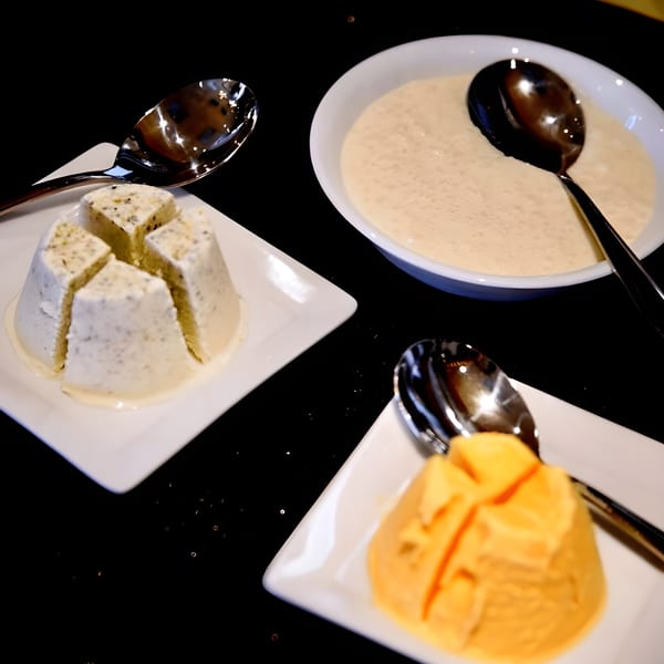 Three Indian desserts, including two sliced kulfi and a bowl of kheer, on a dark surface.